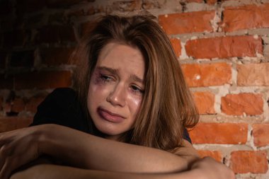 Yaralı genç bir kadın, kasvetli bir ortamda üzüntüsünü ve üzüntüsünü ifade eden tuğla bir duvara yaslanır..