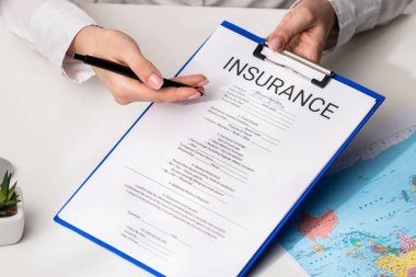 Ofiste seyahat sigortası formunu belgelemek, ajanların ellerini kapatmak. Bir kişi, yanında harita olan bir sigorta formunu panoya dolduruyor. Sahne hazırlığı iletir..