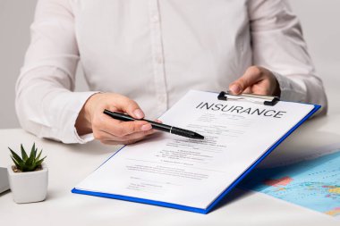 Ofisteki seyahat sigortası formunu belgeliyorum. Bir sigorta acentesi, anlaşmanın detaylarını gözden geçirir ve anlamanın anahtar şartlarını vurgular.