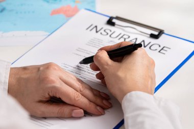 Ofiste seyahat sigortası formunu belgelemek, ajanların ellerini kapatmak. Anlaşmadan önce dikkatle incelenmenin önemini vurgulayan bir sigorta belgesi imzalayan kişi.