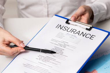 Ofisteki seyahat sigortası formunu belgeliyorum. Bir bireyin sigorta formunu doldururken yakın çekim görüntüsü, önemli alanlar ve belgelerin özelliklerini vurguluyor.