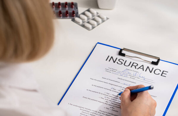 A person is filling out a medical examination form for insurance purposes, carefully writing on the document. Documenting a life and health insurance form in office of a hospital or insurance agency.