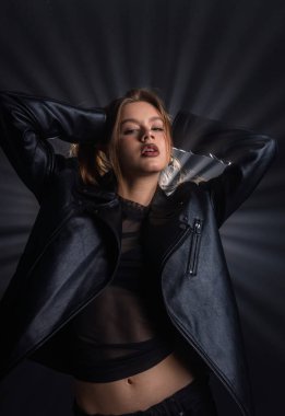 Kendine güvenen bir kadın siyah deri bir ceketle, siluetini aydınlatan ışık ışınlarıyla dramatik bir şekilde poz veriyor. Moda yazıları, giyim markaları veya aksesuar reklamları için..