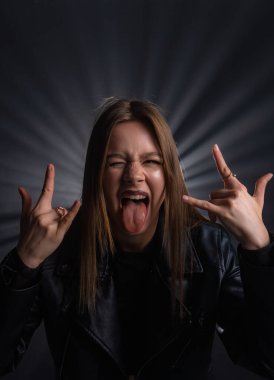 Deri ceketli bir kadın sert bir jest yapar, dilini uzatır, yoğun bir heyecan gösterir. Moda yazıları, giyim markaları veya aksesuar reklamları için..