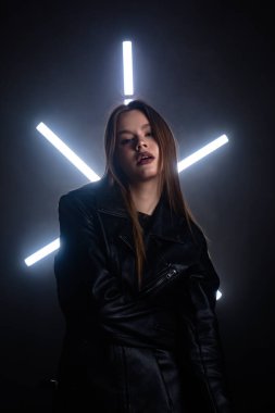 Siyah deri ceketli şık bir kadın dramatik bir ışıklandırma arkaplanına karşı duruyor, karamsar ve sanatsal bir portre oluşturuyor. Moda yazıları, giyim markaları veya aksesuar reklamları için..