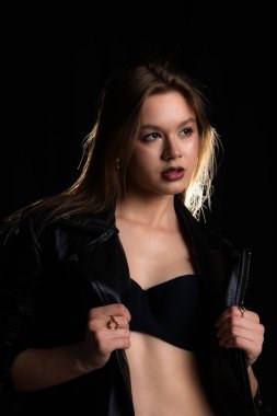 Siyah deri ceketli bir kadın dramatik ışıklandırma altında kendine güvenerek poz verir. Kompozisyon onun ifadesini vurguluyor. Moda yazıları, giyim markaları veya aksesuar reklamları için..