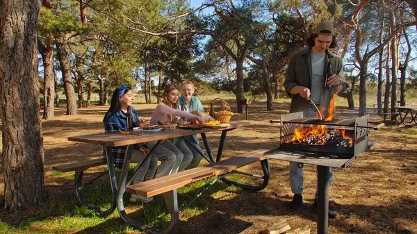 Bir grup arkadaş güneşli bir günün tadını çıkarıyorlar. Uzun ağaçlarla çevrili, pitoresk bir parkta barbekü yapıyorlar..