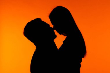 Romantik bir siluet, büyüleyici turuncu bir zemin ile sarılıp, samimiyeti ön plana çıkaran bir çift..