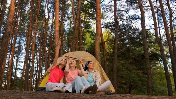 Yoğun bir ormanda çadırda kamp maceralarının keyfini çıkarırken üç kadın gökyüzünü neşeyle işaret ediyor..