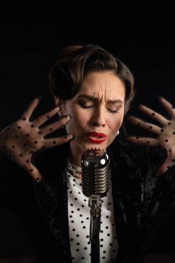 Şık eldivenler ve retro giysiler giymiş klasik bir mikrofonla tutkuyla şarkı söyleyen bir şarkıcı..