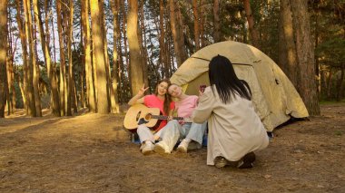 Arkadaşlarla dolu canlı bir kamp sahnesi müzik ve kahkahaların tadını çıkaran yemyeşil bir ormanda doğa ile çevrili..