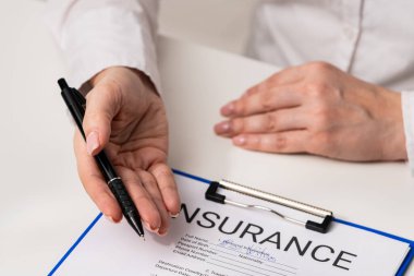 İmzalamaya hazır, sözleşmeli bir anlaşma sürecini gösteren bir sigorta formunun üzerinde kalem tutan bir kişi. Ofisteki seyahat sigortası formunu belgelemek, ajanların ellerini kapatmak..