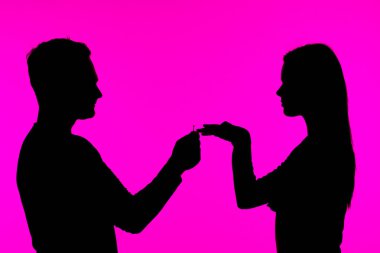 Romantik bir siluet sahnesi, canlı pembe bir fon tarafından vurgulanmış bir adamın bir kadına evlenme teklif edişini gösteriyor..