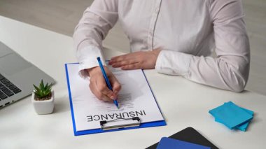 Sigorta belgesinin yanında elinde kalem tutan bir kişinin yakın plan fotoğrafı, önemini vurgulamak için. Ofiste sigorta formunu belgelemek.