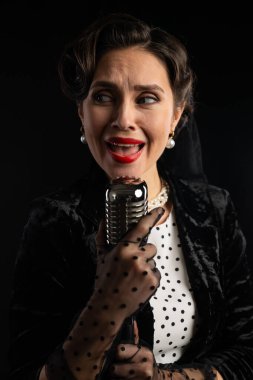 Eski bir mikrofona zarif bir şekilde şarkı söyleyen bir kadın, üzerinde puantiyeli ve incili siyah kadife bir kıyafet, klasik bir retro titreşim yakalıyor..