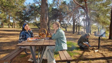 Ormanlık bir parkta piknik yapan bir grup arkadaş, doğada yemek ve sohbetin tadını çıkarıyorlar..