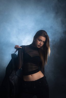 Karamsar, dumanlı bir arka plan üzerine kurulmuş, koyu moda giyinmiş bir kadının çarpıcı portresi. Görüntü gizem ve stil duygusunu yakalar. Moda yazıları, giyim markaları veya aksesuar reklamları için..