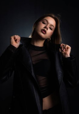 Siyah deri ceketli bir kadın, moda fotoğrafçılığında kendine güveni ve stili somutlaştıran koyu bir arka plana karşı poz veriyor. Moda yazıları, giyim markaları veya aksesuar reklamları için..