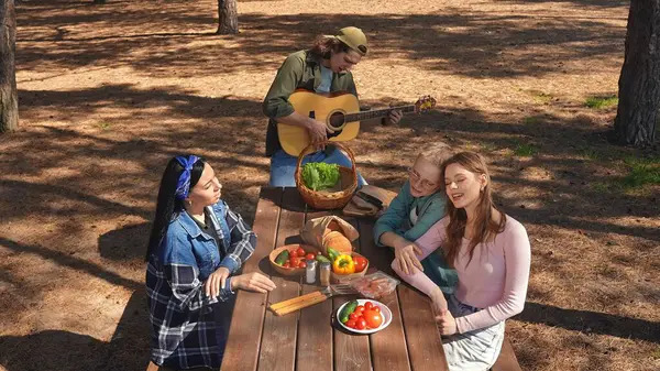 Bir grup arkadaş piknik için toplanır, güneşli bir açık hava ortamında yemek ve müziğin tadını çıkarırlar, rahatlamayı teşvik ederler..