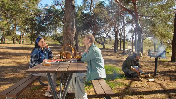 Ormanlık bir parkta piknik yapan bir grup arkadaş, doğada yemek ve sohbetin tadını çıkarıyorlar..