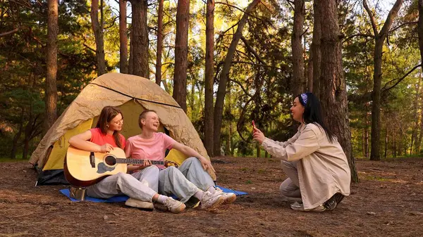 Arkadaşlarla dolu canlı bir kamp sahnesi müzik ve kahkahaların tadını çıkaran yemyeşil bir ormanda doğa ile çevrili..