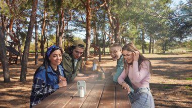 Bir grup arkadaş, orman ortamında piknikte harika vakit geçiriyorlar. Anları yakalamak için telefon kullanıyorlar..