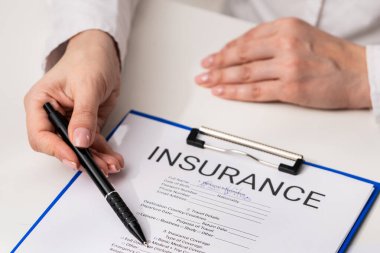 Sigorta belgesinin yanında elinde kalem tutan bir kişinin yakın plan fotoğrafı, önemini vurgulamak için. Ofiste sigorta formunu belgelemek.