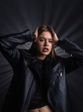 Şık bir deri ceket giyen bir kadının çarpıcı portresi. Karanlık arka plan ve sanatsal ışıklandırma onun ifadesini vurguluyor. Moda yazıları, giyim markaları veya aksesuar reklamları için..
