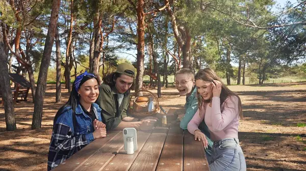 Bir grup arkadaş, orman ortamında piknikte harika vakit geçiriyorlar. Anları yakalamak için telefon kullanıyorlar..