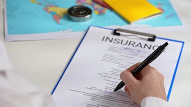Ofiste seyahat sigortası formunu belgelemek, ajanların ellerini kapatmak. Bir kişi, anlaşmaların güvence altına alınmasında dikkatli belgelerin önemini vurgulayan önemli sigorta belgelerini imzalar.