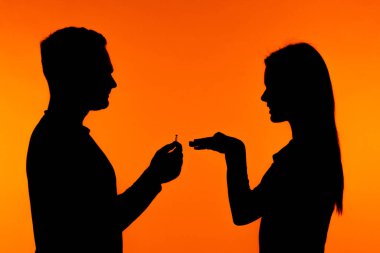 Romantik bir siluet, canlı turuncu bir arkaplan karşısında bir kadına evlenme teklif eden bir adam. Sahne, samimi anı güzel bir şekilde yakalar..