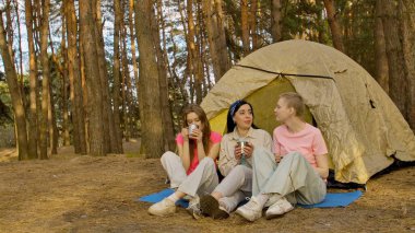Üç arkadaş ormanda bir çadırda oturup, bir kamp gezisi sırasında içkinin ve arkadaşlığın tadını çıkarıyorlar..