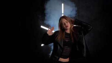 Siyah deri ceketli biri arka planda neon ışıklarla poz verip dramatik ve şık bir görünüm yaratıyor. Moda yazıları, giyim markaları ya da aksesuar reklamları için. Yavaş çekim.