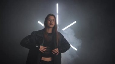 Siyah deri ceketli biri arka planda neon ışıklarla poz verip dramatik ve şık bir görünüm yaratıyor. Moda yazıları, giyim markaları ya da aksesuar reklamları için. Yavaş çekim.