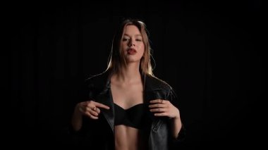 Siyah deri ceketli bir kadın koyu bir arka plana karşı özgüvenle poz verir, zarafet ve tarz yayar. Moda yazıları, giyim markaları veya aksesuar reklamları için..