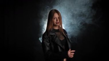 Siyah deri ceketli bir kadın koyu bir arka plana karşı özgüvenle poz verir, zarafet ve tarz yayar. Moda yazıları, giyim markaları veya aksesuar reklamları için..