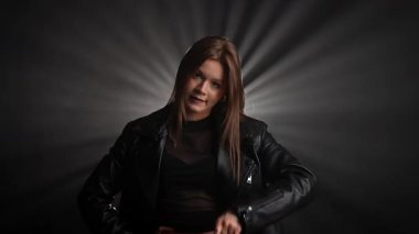 Siyah deri ceketli bir kadın koyu bir arka plana karşı özgüvenle poz verir, zarafet ve tarz yayar. Moda yazıları, giyim markaları veya aksesuar reklamları için..