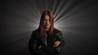 Siyah deri ceketli bir kadın koyu bir arka plana karşı özgüvenle poz verir, zarafet ve tarz yayar. Moda yazıları, giyim markaları veya aksesuar reklamları için..