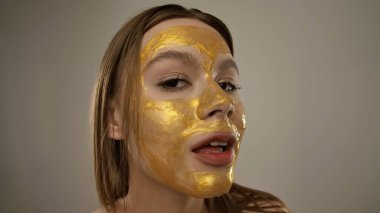 Bir kadın altın renkli bir maske takar. Işıl ışıl ve ışıl bir cildi teşvik eder. Güzelliği ve sağlığı arttırır..