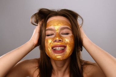 Bir kadın, altın maskeli, cildini güzelleştiren bir güzellik rutiniyle neşeyle şımarır..