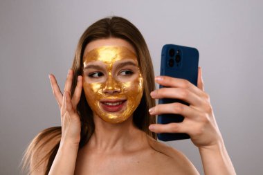 Bir kadın lüks bir altın yüz maskesi takar ve akıllı telefonunda bir selfie ile o anı yakalar..