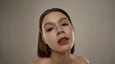 Yanağına yüz kremi sürerken gülümseyen bir kadın, rutin cilt bakımını gösterir..