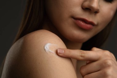 Bir kadın omzuna nazikçe nemlendirici sürerek günlük cilt bakımında önemli bir adımın altını çizer..