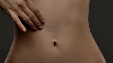 Bir kadın eli karnına krem sürüyor.