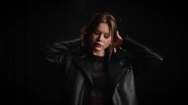 Siyah deri ceketli bir kadın koyu bir arka plana karşı özgüvenle poz verir, zarafet ve tarz yayar. Moda yazıları, giyim markaları veya aksesuar reklamları için..