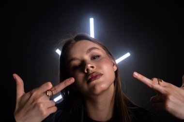 Küstah bir kadın, parlak ışıklarla loş bir odada, kendinden emin bir şekilde orta parmağını kaldırır. Moda yazıları, giyim markaları veya aksesuar reklamları için..