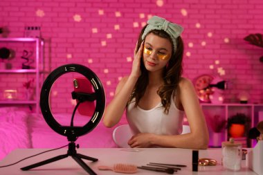 Bir güzellik blogcusu cilt bakımını gösterirken göz bandı altında altın yapıştırıyor. Mekan canlı ve neşeli..