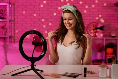 Neşeli bir birey makyaj masasında oturuyor. Güzellik ürünleriyle çevrili. Büyüleyici bir video seansına hazır..