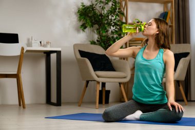 Genç bir kadın su içmek için yoga seansına ara veriyor. Odaklanma ve su kaybını arttırıyor..