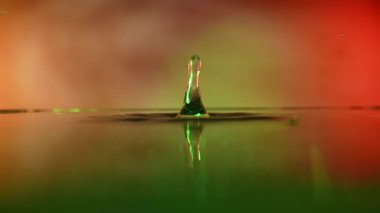 Bir su damlasını canlı renklerde yakalayan büyüleyici bir görüntü, karmaşık yansımalar ve yüzey gerilimi sergiliyor..